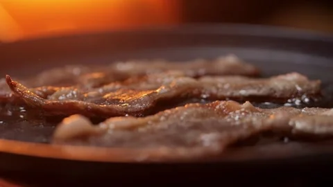 Fresh, delicious bacon slices are sizzling in a hot pan, showcasing flavorful Stock Footage 306015553
