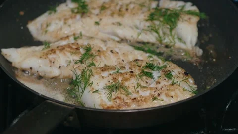Fresh dill sprinkled over cod fillets as they sear in a skillet Video stock 324752429