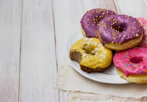 Fresh donuts with colorful glaze in the white plate on the wooden background Stock Photos