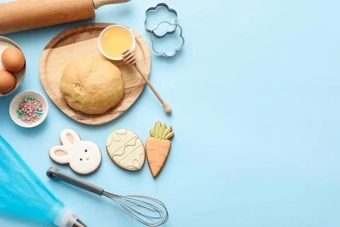 Fresh dough with Easter cookies, eggs, honey and kitchen utensils on blue bac Stock Photos