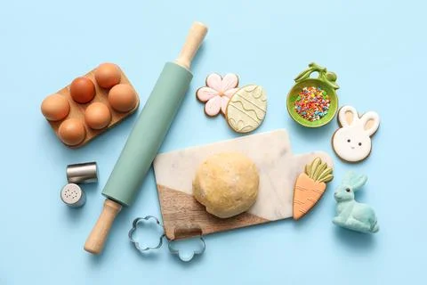 Fresh dough with Easter cookies, eggs and kitchen utensils on blue background Stock Photos