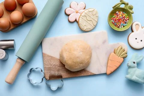 Fresh dough with Easter cookies, eggs and kitchen utensils on blue background Stock Photos