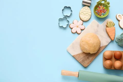 Fresh dough with Easter cookies, eggs and kitchen utensils on blue background Stock Photos
