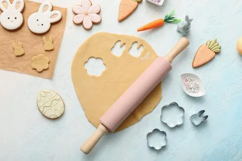 Fresh dough with raw Easter cookies and kitchen utensils on light blue backgr Stock Photos