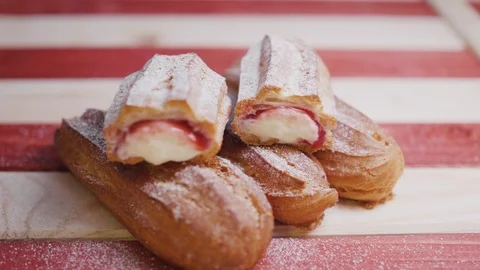 Fresh eclairs lying on a red and white striped wooden tray, sprinkling with Stock Footage 105485552