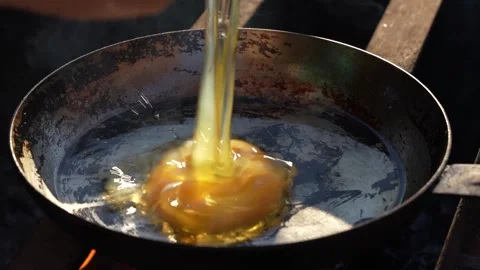 Fresh egg is fried in frying pan outdoors with oil and smoke on open fire Stock Footage 299309669
