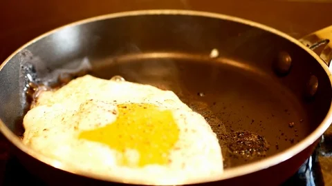Fresh egg with ground pepper is frying in a hot fry pan as steam rises. Close. Stock Footage 103398840