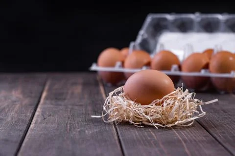A fresh egg on the straw, with a full package of eggs in the background. Wood Stock Photos