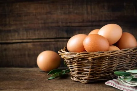 Fresh eggs in a rustic willow basket against dark wooden background Stock Photos