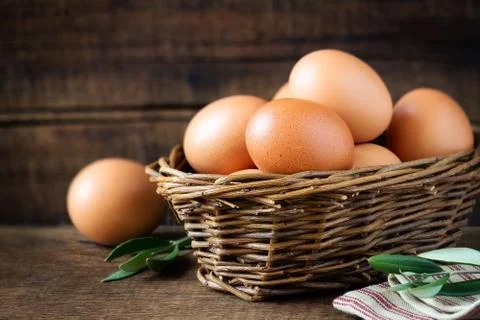Fresh eggs in a rustic willow basket against dark wooden background Stock Photos