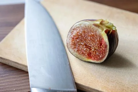 Fresh fig sliced in half with a chef knife on a rustic wooden board Stock Photos