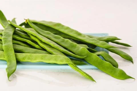 Fresh flat green beans placed on a blue tray. Stock Photos