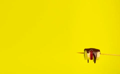 Fresh fruit drenched in liquid chocolate on a stick. Yellow background and pl Stock Photos
