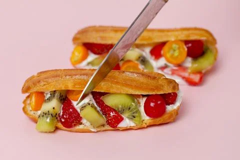 Fresh fruit eclairs on a pink surface with a knife cutting one Stock Photos
