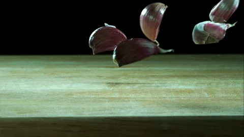 Fresh garlic cloves fall and bounce on wooden board Stock Footage 327581248