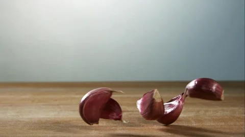Fresh garlic cloves falling and bouncing on wooden table Stock Footage 327577862