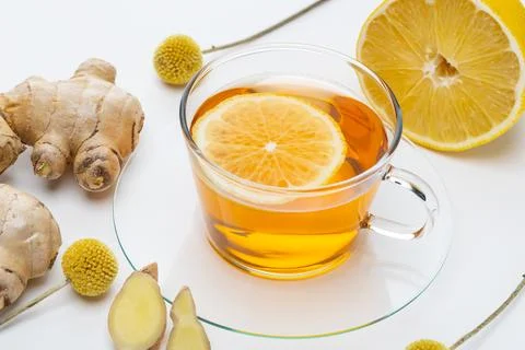 Fresh ginger tea with lemon slice on a white surface alongside ginger roots.. Stock Photos