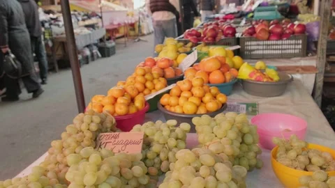 Fresh grapes, apples, persimmons displayed in foreground at open-air market Stock Footage 323723795