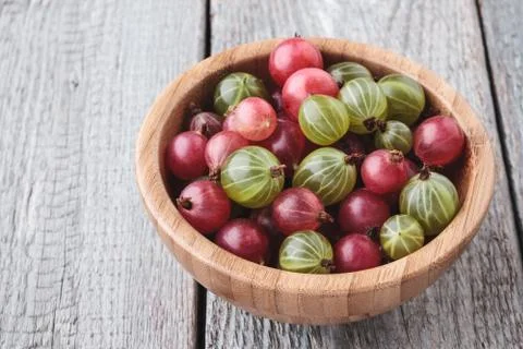 Fresh green and red gooseberries in a bamboo bowl on a wooden table. Top view Stock Photos