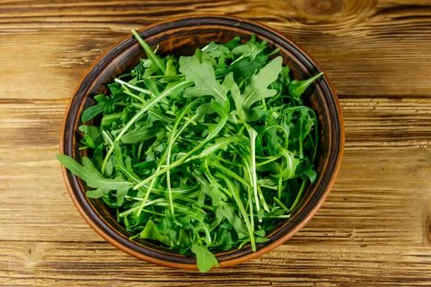 Fresh green arugula in ceramic bowl on a wooden table. Stock Photos