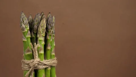 Fresh green asparagus rotates on a brown background. healthy food concept Stock Footage 242169727