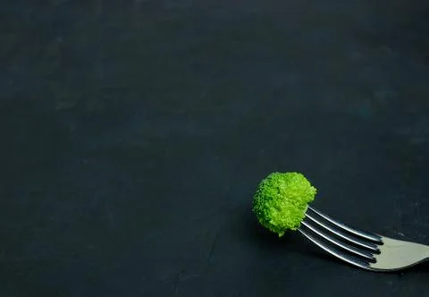 Fresh green broccoli on the fork. Pattern healthy eating on a dark background Stock Photos