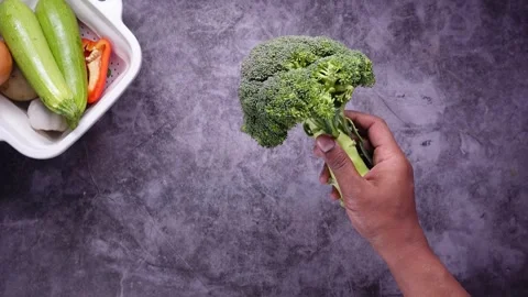Fresh green broccoli held in hand over dark background with assorted vegeta.. Video stock 331934222