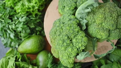 Fresh green broccoli rotates close up against backdrop of lettuce, avocado Stock Footage 340026652