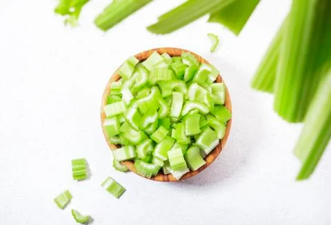 Fresh green celery chopped pieces in bowl, white background, top view, copy s Stock Photos