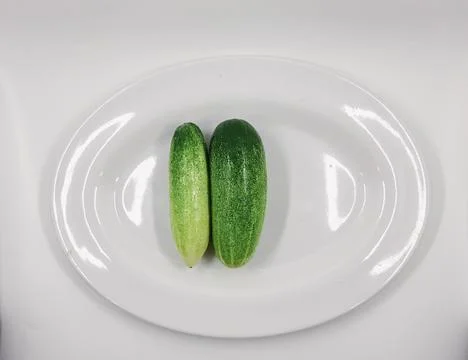 Fresh green cucumbers displayed side by side on a clean white plate. Foto stock