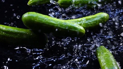 Fresh green cucumbers, falling on black surface with shallow water in back-light Stock Footage 78348675