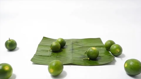Fresh green key limes spread on a banana leaf on a clean white background Stock Footage 306118158