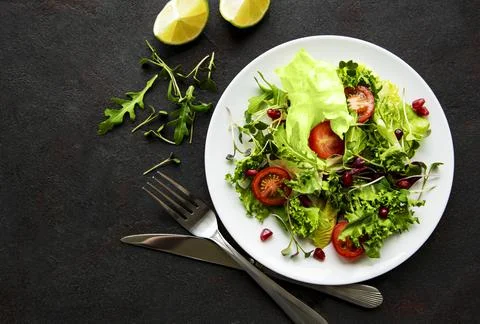 Fresh green mixed  salad bowl with tomatoes and microgreens  on black concret Stock Photos