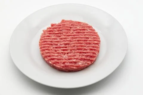 Fresh ground beef patty ready for grilling in a white dish. Stock Photos