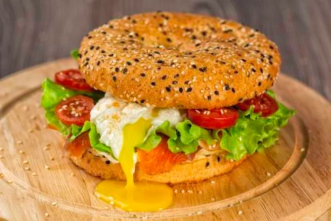 Fresh healthy bagel with salmon, lettuce, tomatoes and soft egg on a round board Stock Photos
