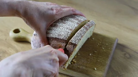 Fresh homemade bread is hand sliced on a wooden board Stock Footage 335327131