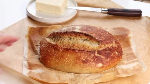 Fresh homemade bread loaf with crispy golden crust resting on parchment paper Stock Footage 311511334