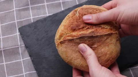 Fresh homemade bread loaf held by hands on black slate highlighting rustic Video stock 311511194