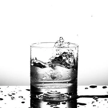 Fresh ice cube falling to glass of water splash isolated Stock Photos