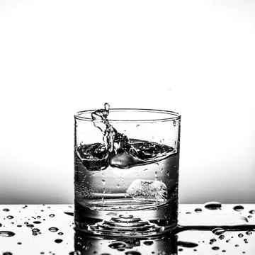 Fresh ice cube falling to glass of water splash isolated Stock Photos