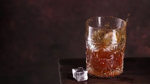 Fresh ice cubes are dropped into glass with whisky 库存影片 143244084