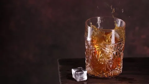 Fresh ice cubes are dropped into glass with whisky 库存影片 143244087