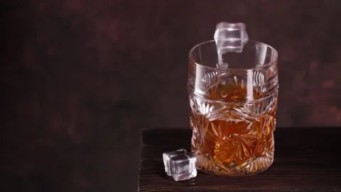 Fresh ice cubes are dropped into glass with whisky Stock Footage 143244092
