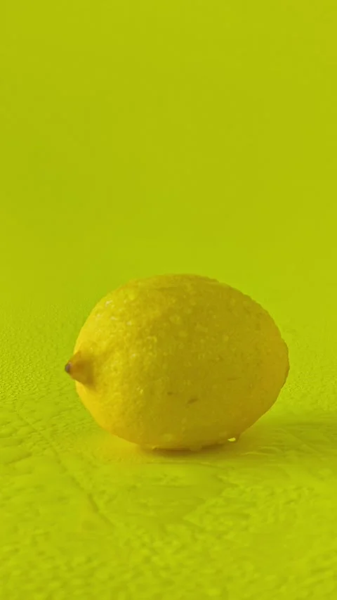 Fresh lemon on a yellow background, splashed with water as glossy droplets. Stock Footage 338182413