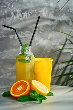 Fresh lemonade in composition with orange and paper cup. Gray background. Stock Photos