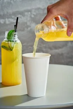 Fresh lemonade poured into a paper cup. Gray background. Stock Photos