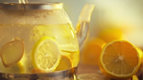 Fresh lemons and raw ginger steep in a glass teapot releasing their zest and Stock Footage 331353581