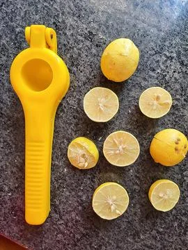 Fresh lemons placed alongside a bright yellow lemon squeezer Stock Photos