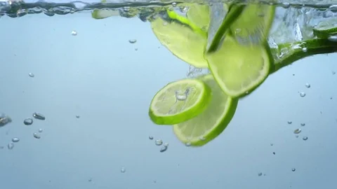 Fresh lime slices fall Into water and float with bubbles slow motion. Stock Footage 76553789