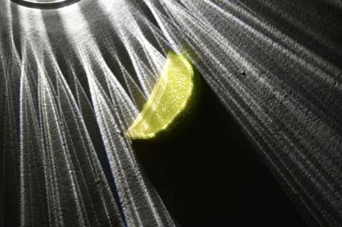 Fresh Lime Wedge with Dramatic Glass Refraction Shadows on Dark Surface Stock Photos